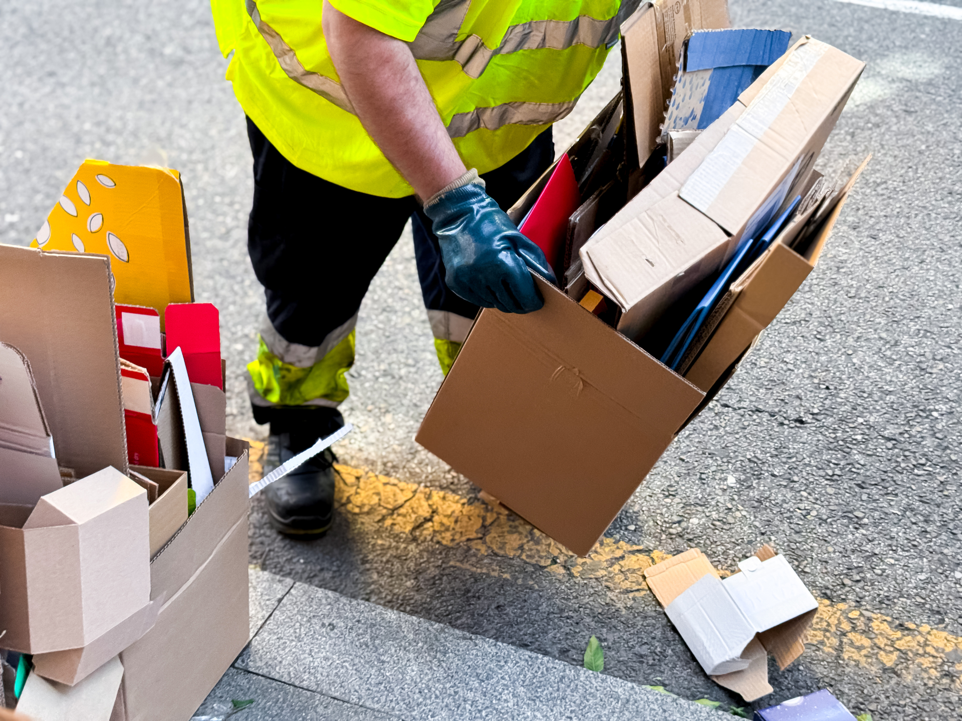 Male worker collecting cardboard boxes for recycling on street