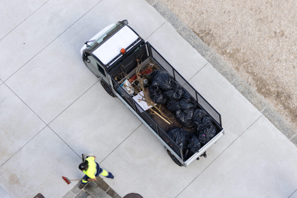 Aerial view of a Electric vehicle loaded with garbage bags and a street cleaner working to collect trash in a city beach area